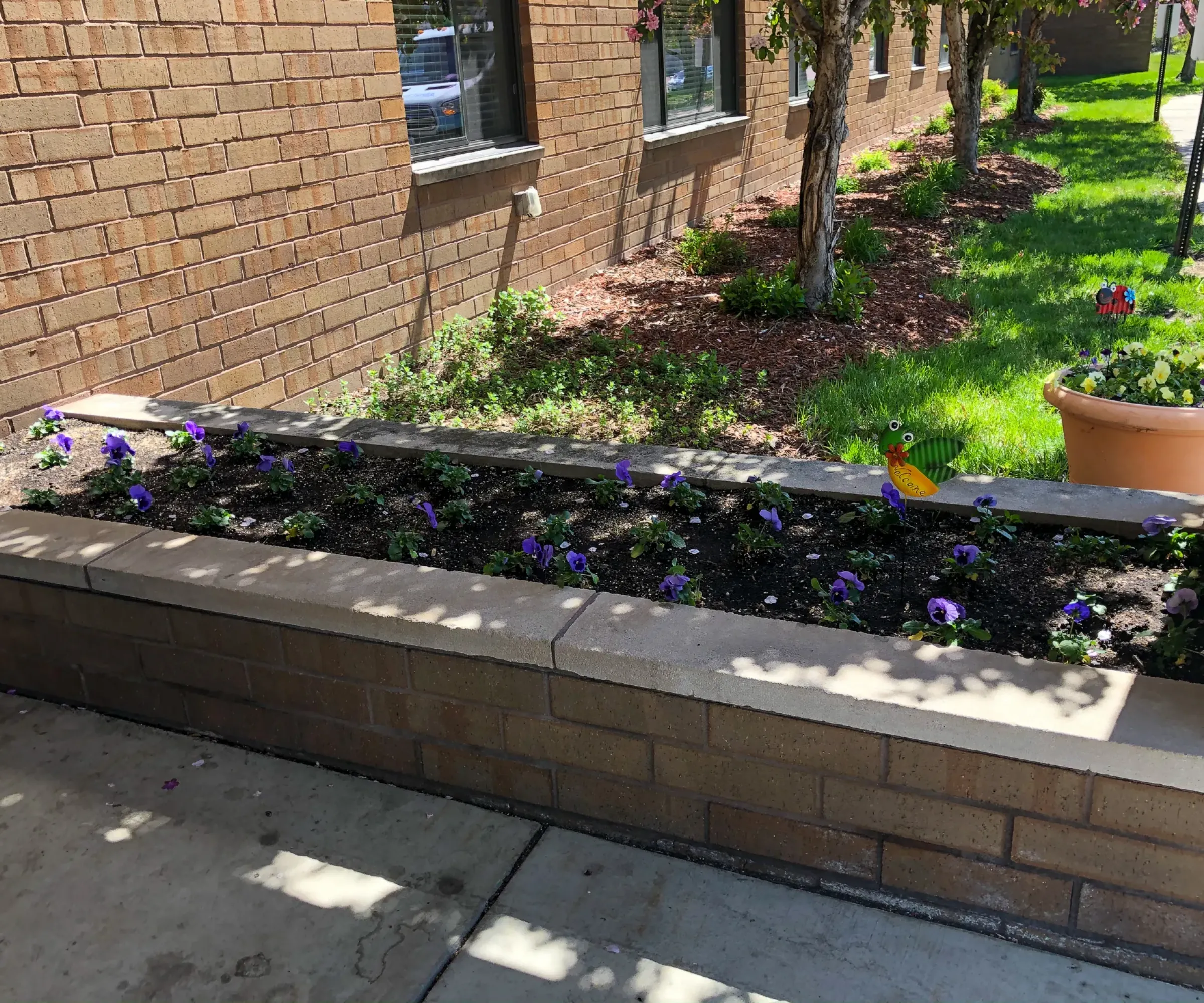 Aeon Affordable Homes and Community A brick planter with purple flowers and a whimsical bird decoration adds charm to the grassy walkway of our affordable apartment homes.