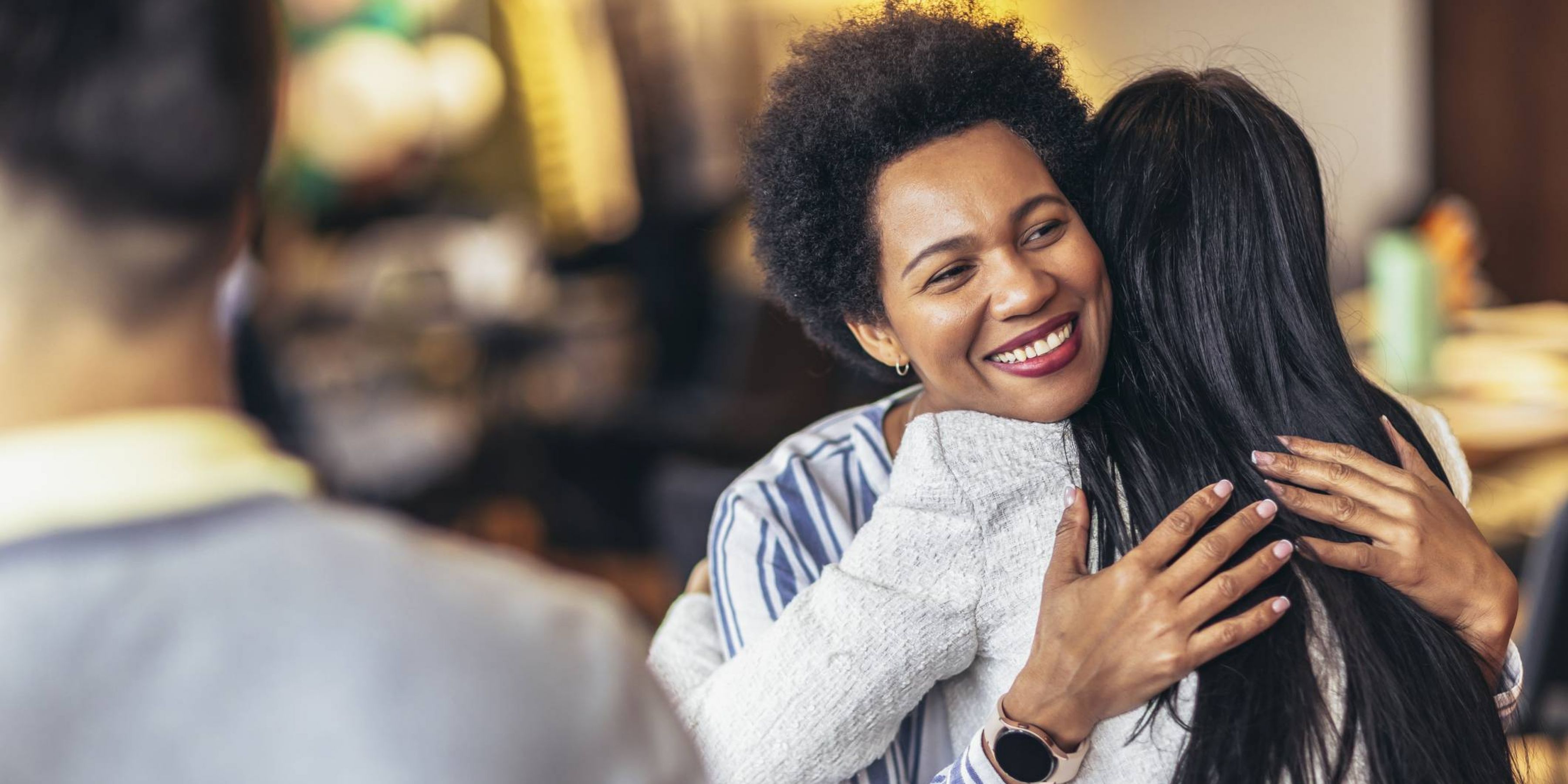 Aeon Affordable Homes Two people hugging warmly in a casual indoor setting, with two others in the background.