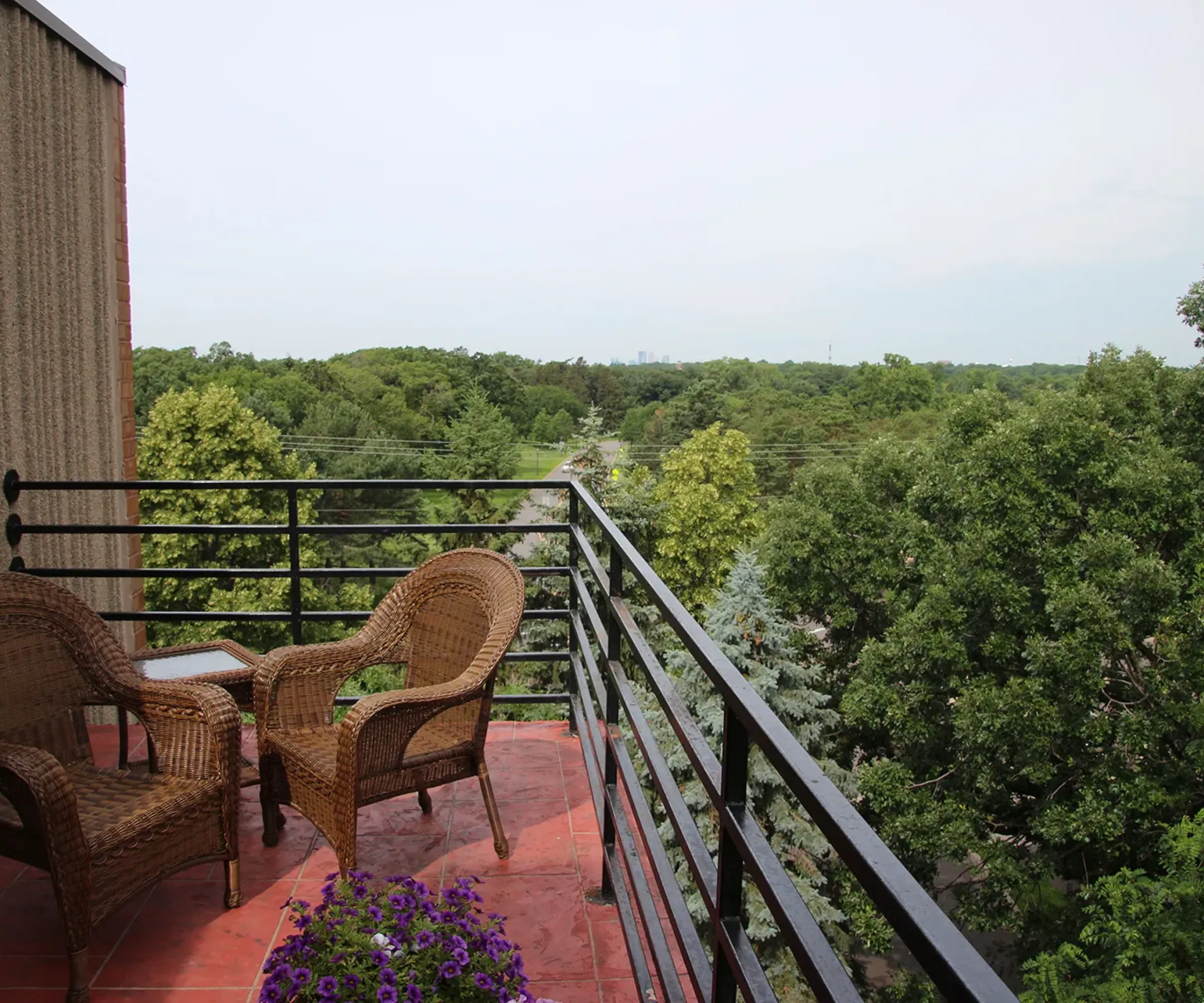 Aeon Affordable Homes and Community Rooftop of affordable apartment homes with wicker chairs and a small table, overlooking lush green trees and a distant horizon.